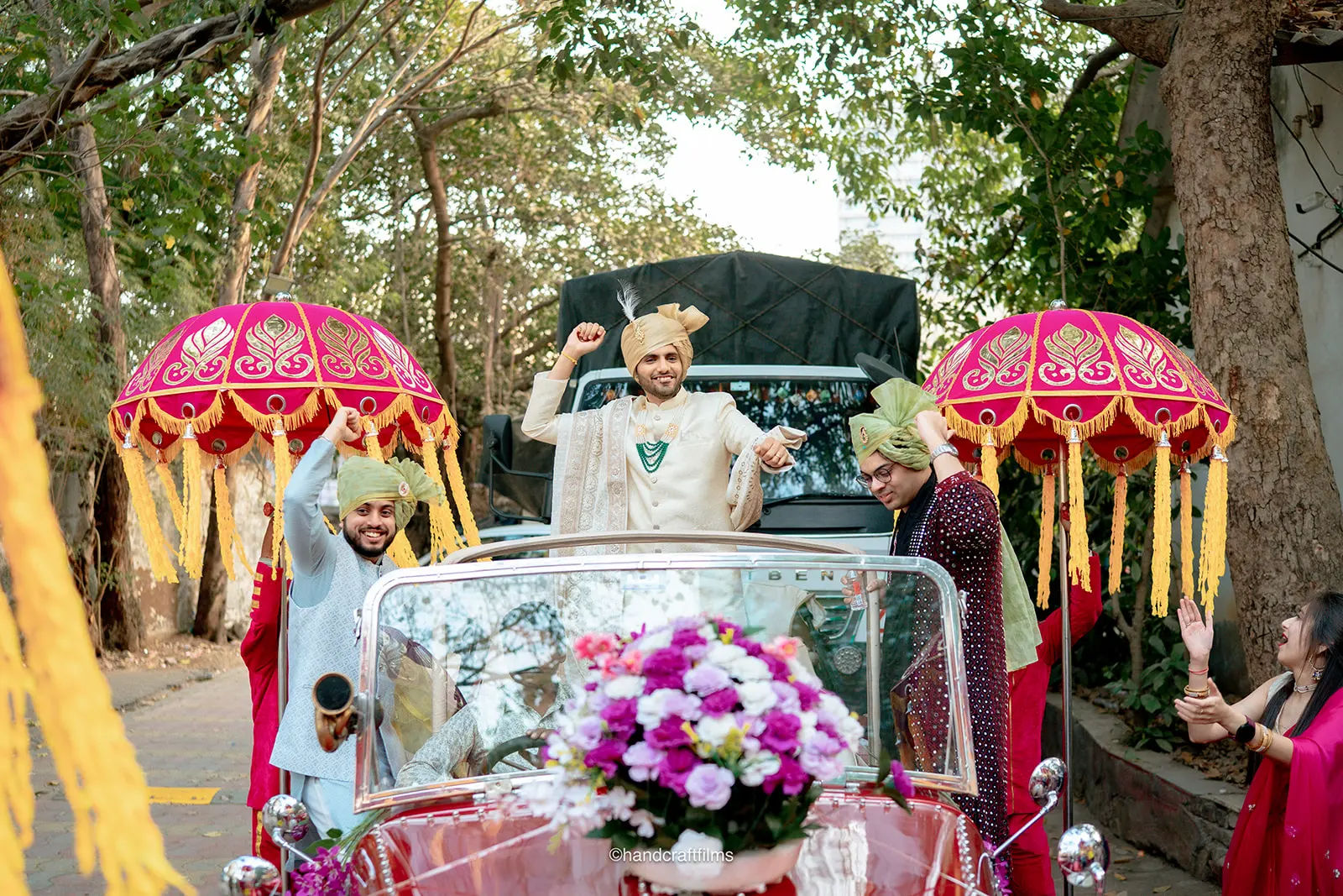Groom standing in a vintage red car during his daytime Baraat