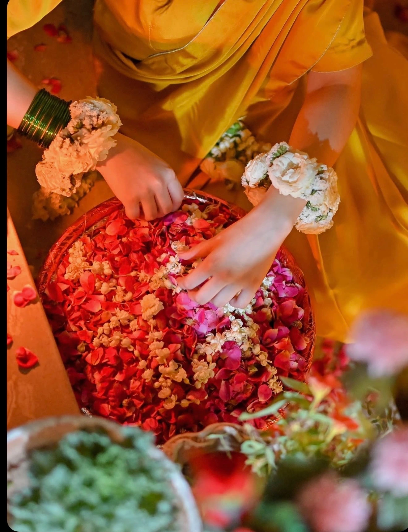Hands with floral bangles gathering rose petals and flowers during a pre-wedding ritual